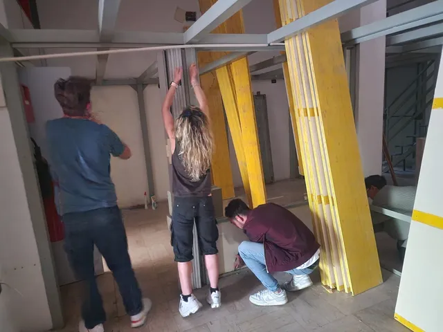 Tre persone assemblano la struttura del controsoffitto con pannelli gialli